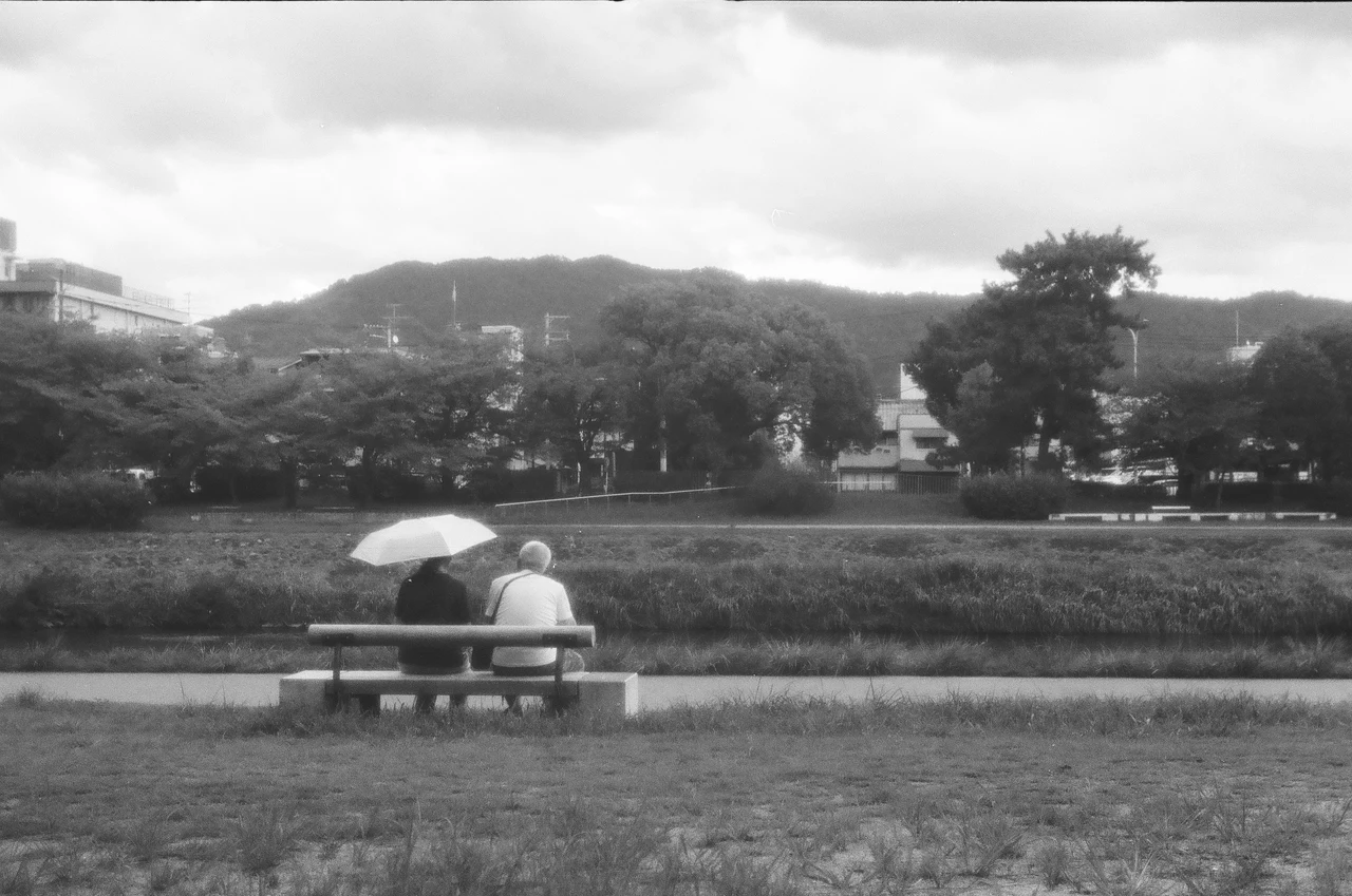 川沿いのベンチで日傘を差す二人